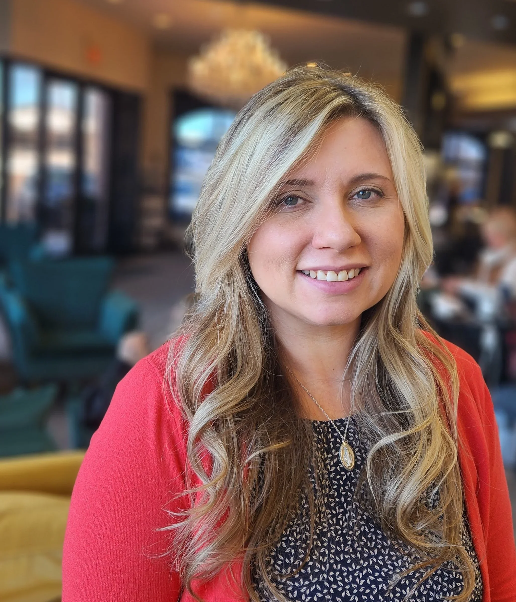 A woman with long, wavy blonde hair smiling indoors