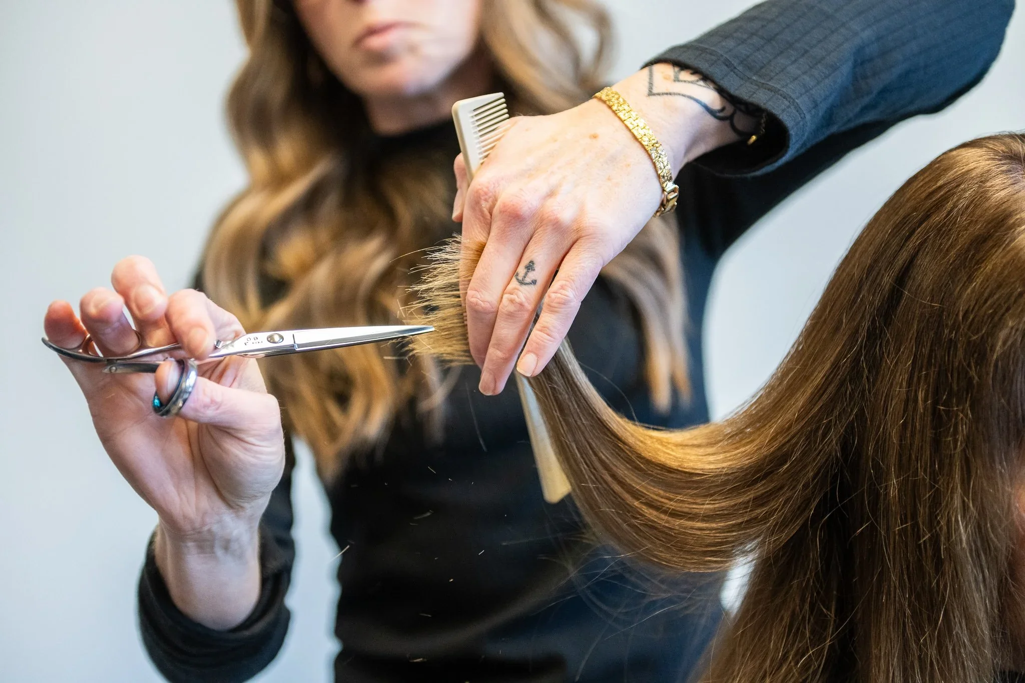 A hairstylist cutting a woman's long, brown hair with scissors