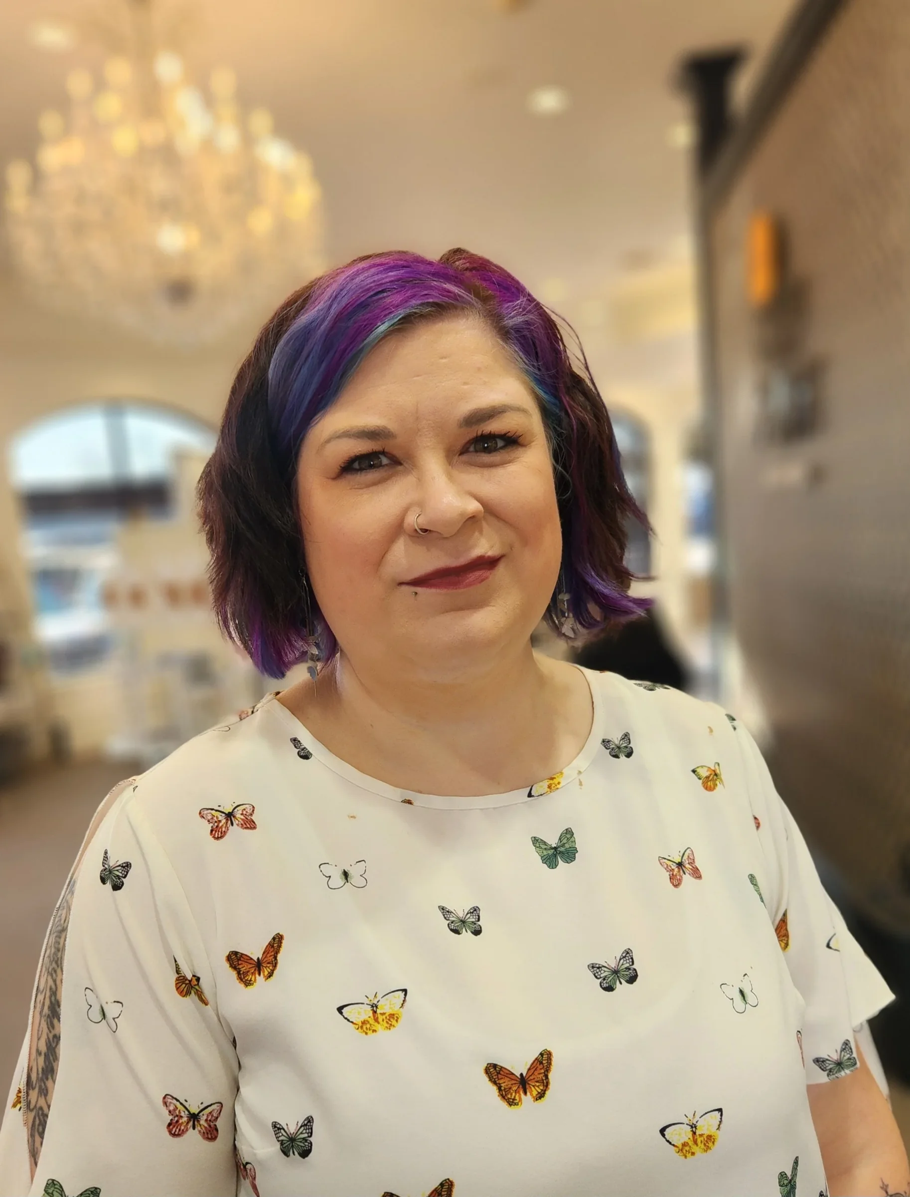 Woman with purple hair and a butterfly shirt standing in salon