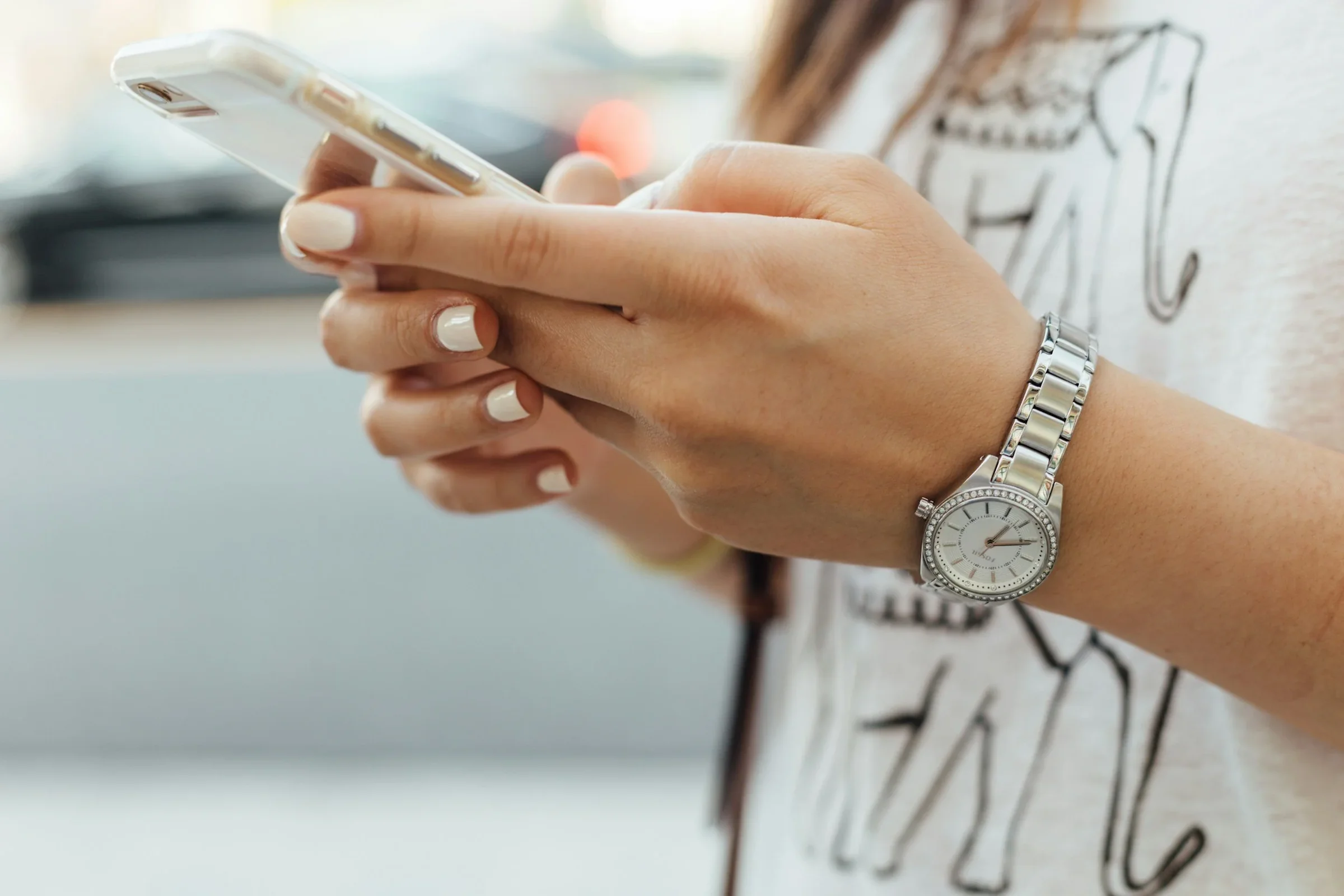 A woman wearing a silver wristwatch, holding a smartphone