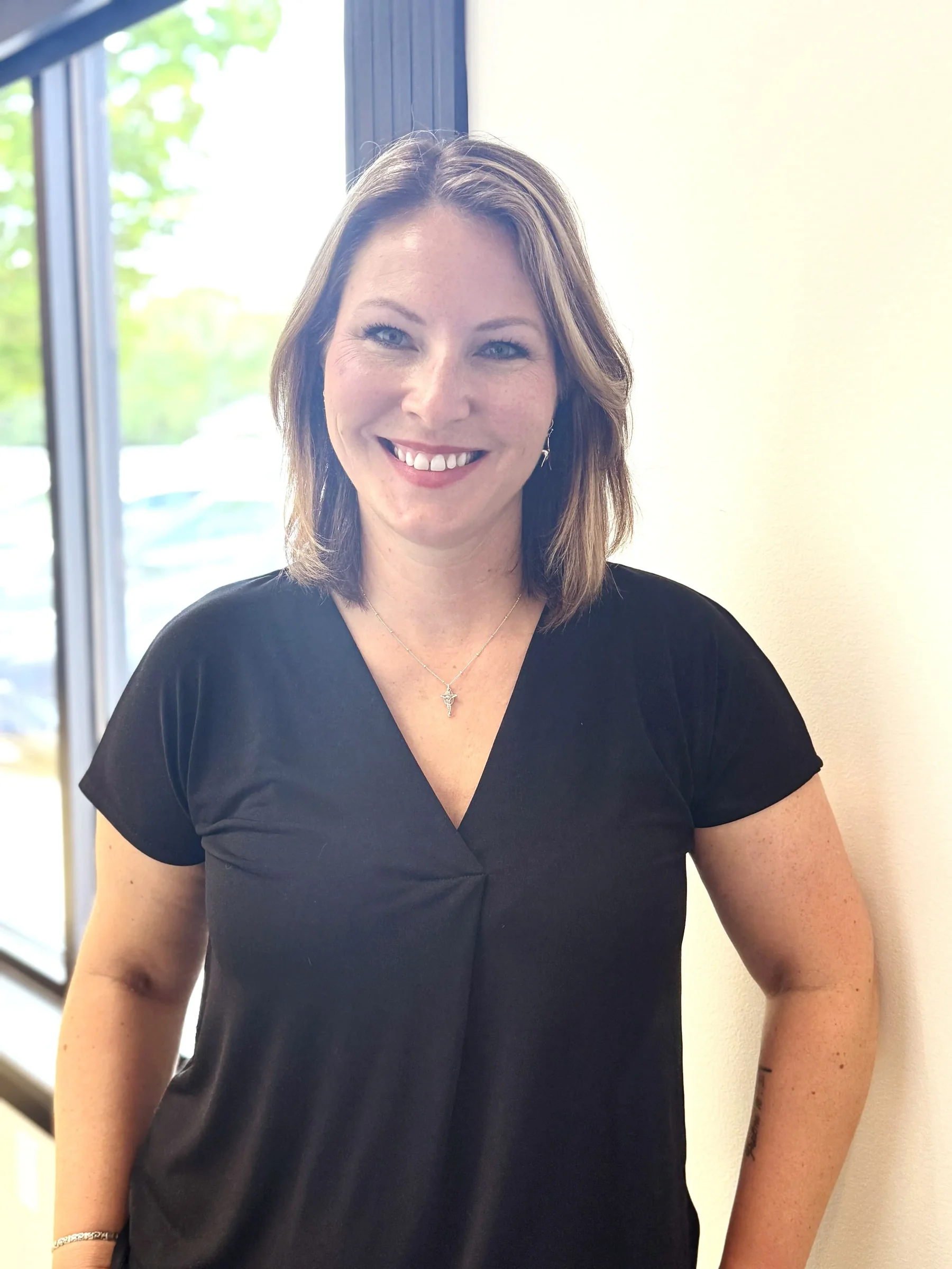 Smiling woman with shoulder-length brown hair, wearing a black V-neck shirt