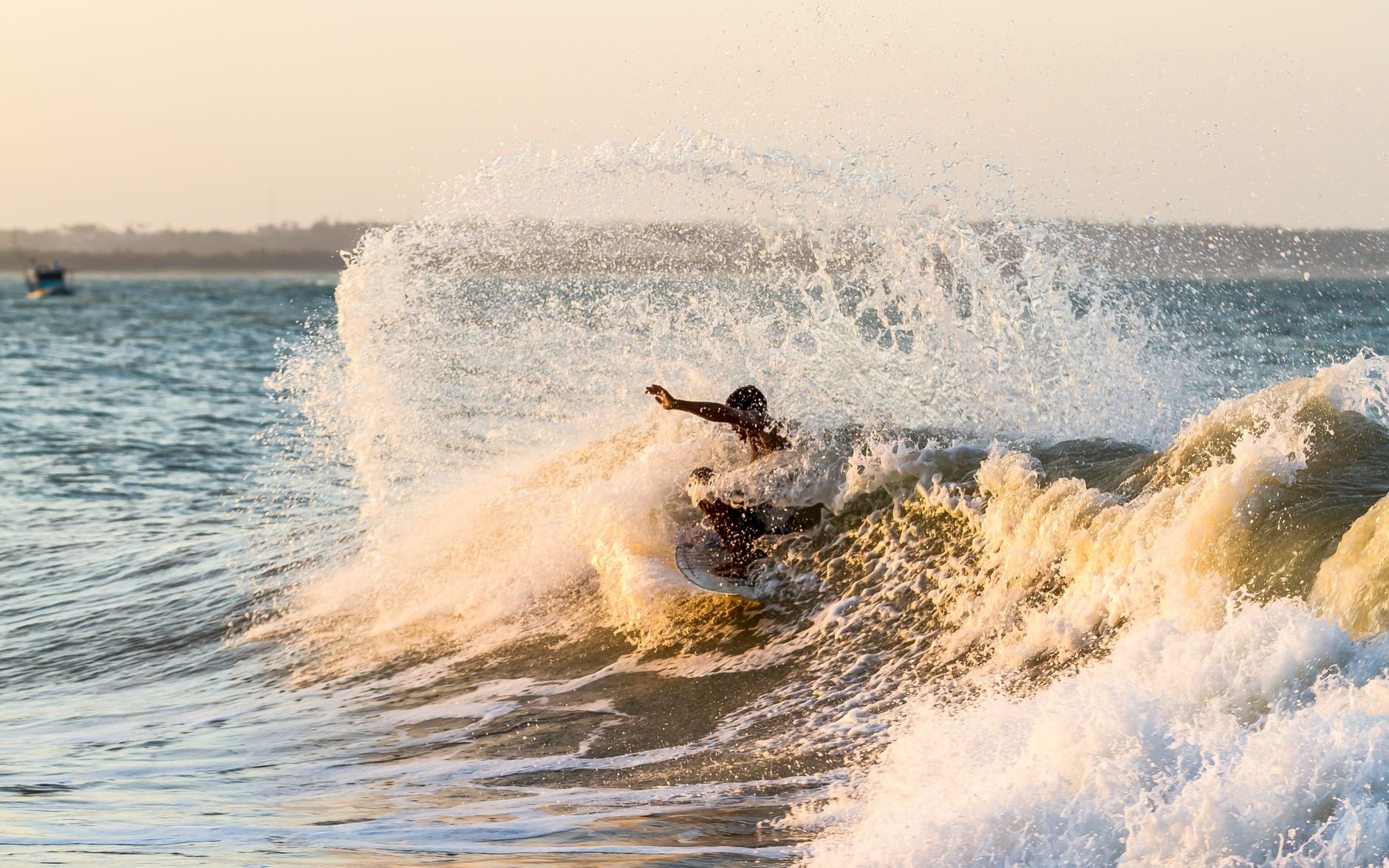 Surfer riding a wave at sunset with dramatic ocean spray
