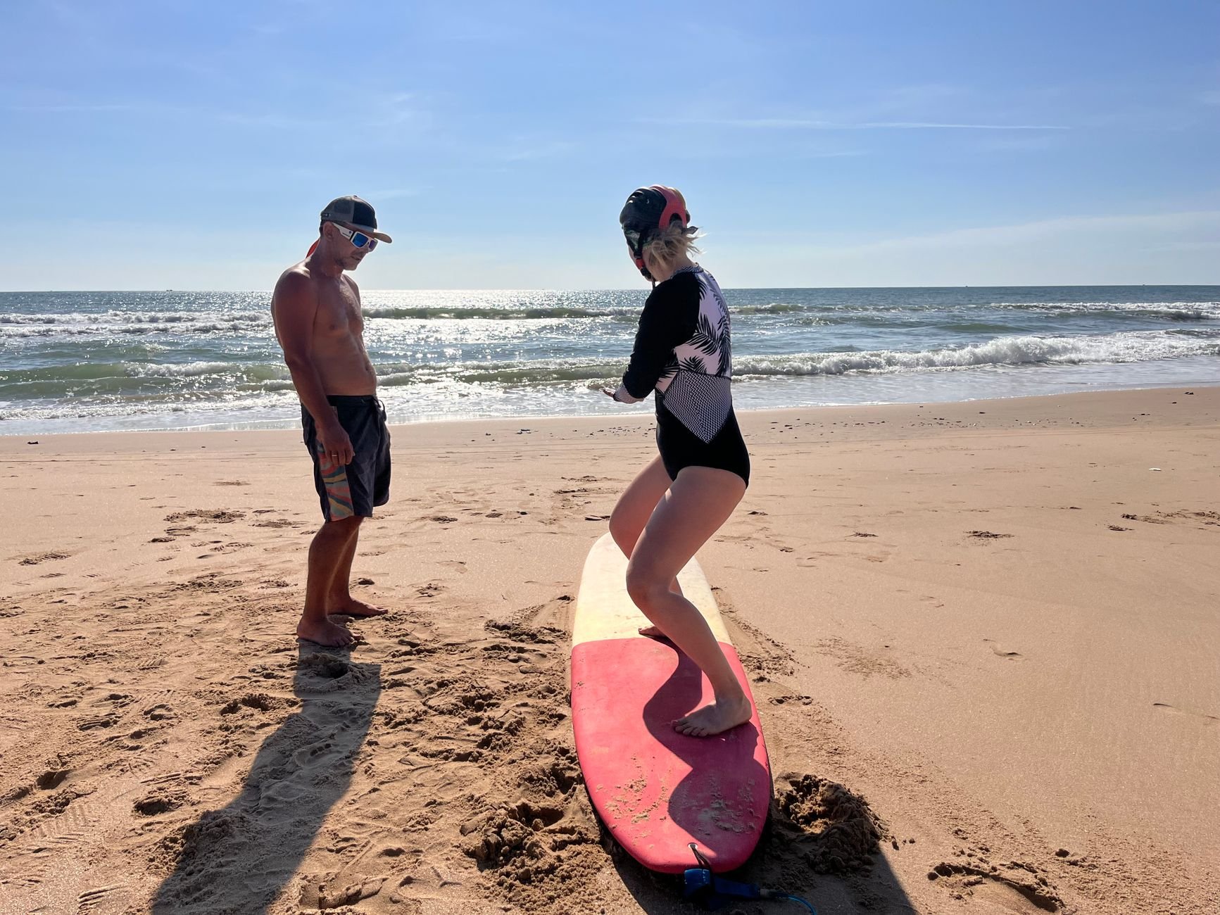A woman learning to surf with an instructor on a sunny beach day